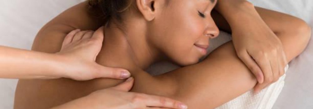 African-american woman enjoying shoulder massage, lying with closed eyes in spa center