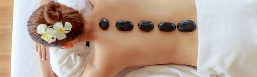 Top view of  young beautiful woman receiving hot black marble stone massage and relaxing in spa salon